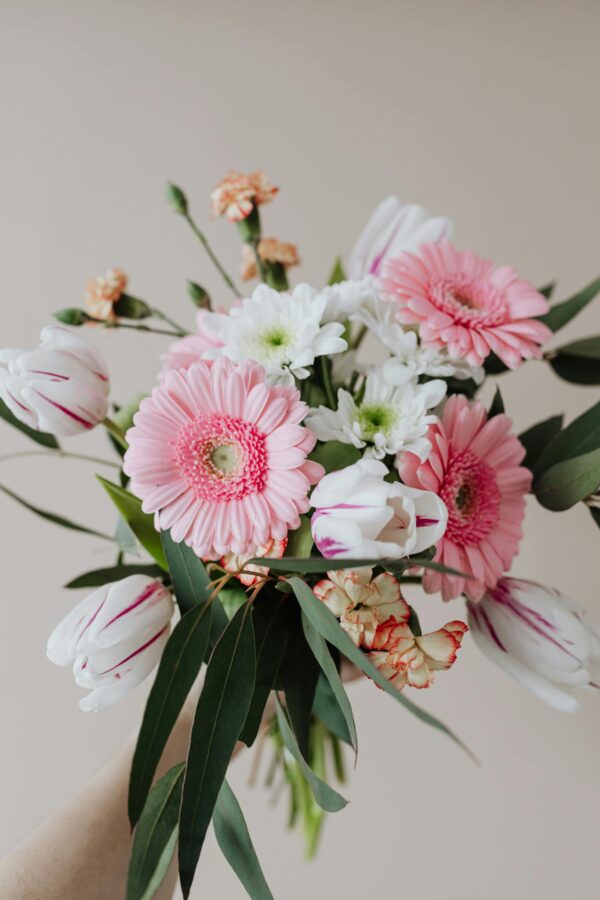 Florist holding blooming chamomiles cloves gerberas and tulips in tender bouquet